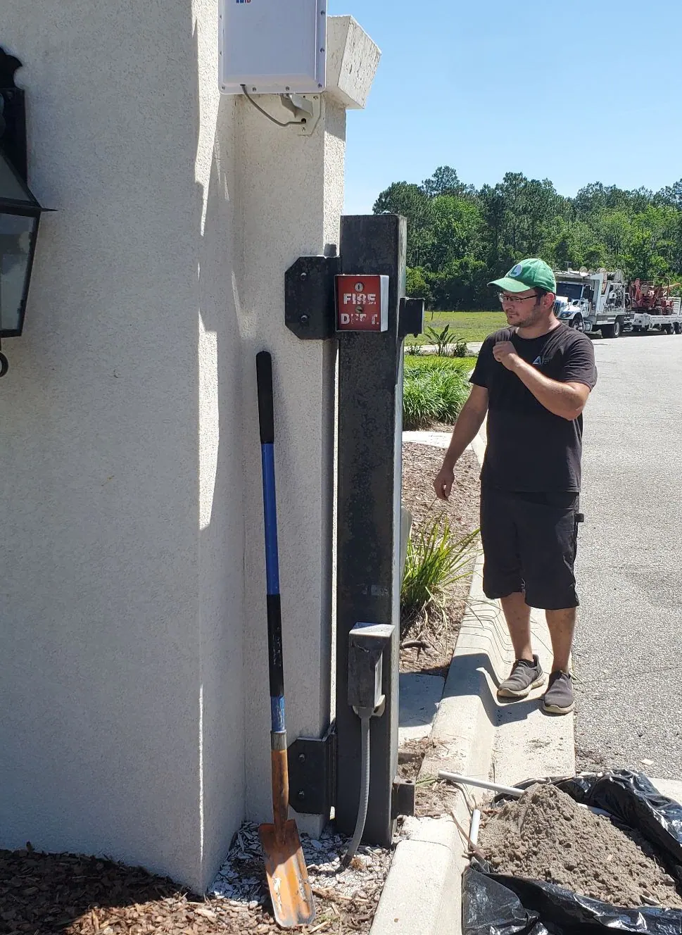 Man in a green cap beside a gate control post at a property entrance
