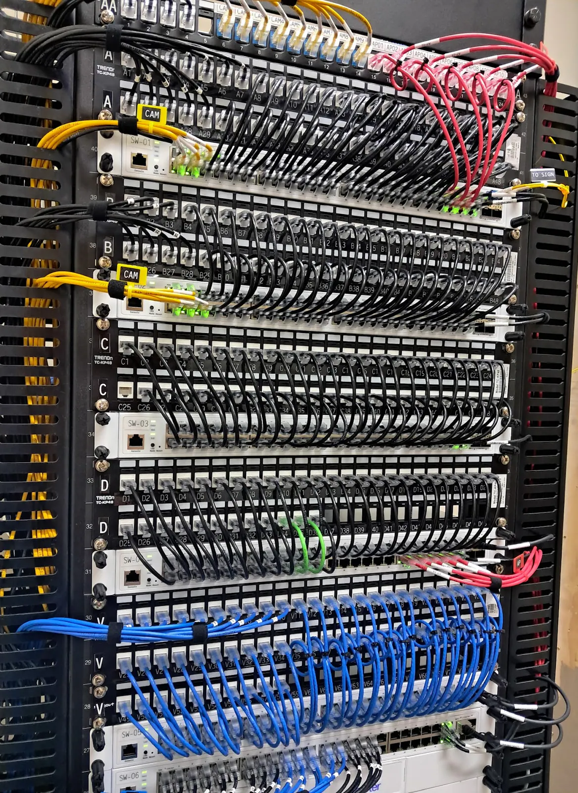Tall network rack with patch panels and yellow and red patch cords