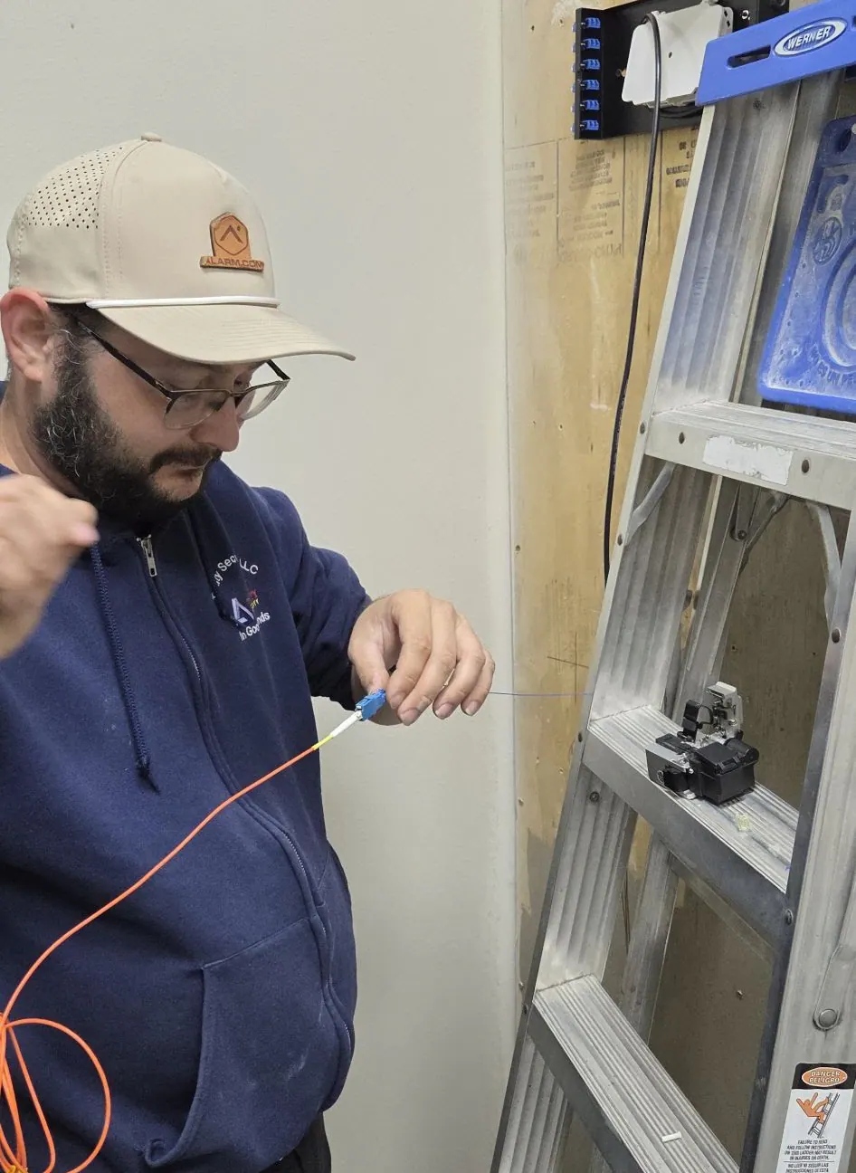Technician with an orange fiber cable beside a ladder
