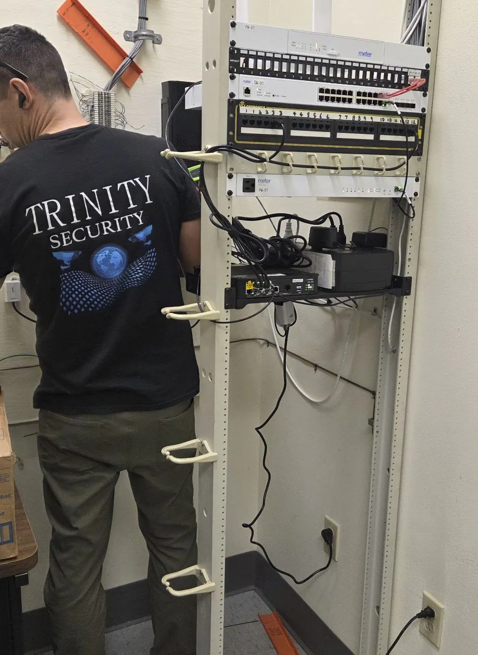 Technician in a Trinity Security shirt beside a wall-mounted rack
