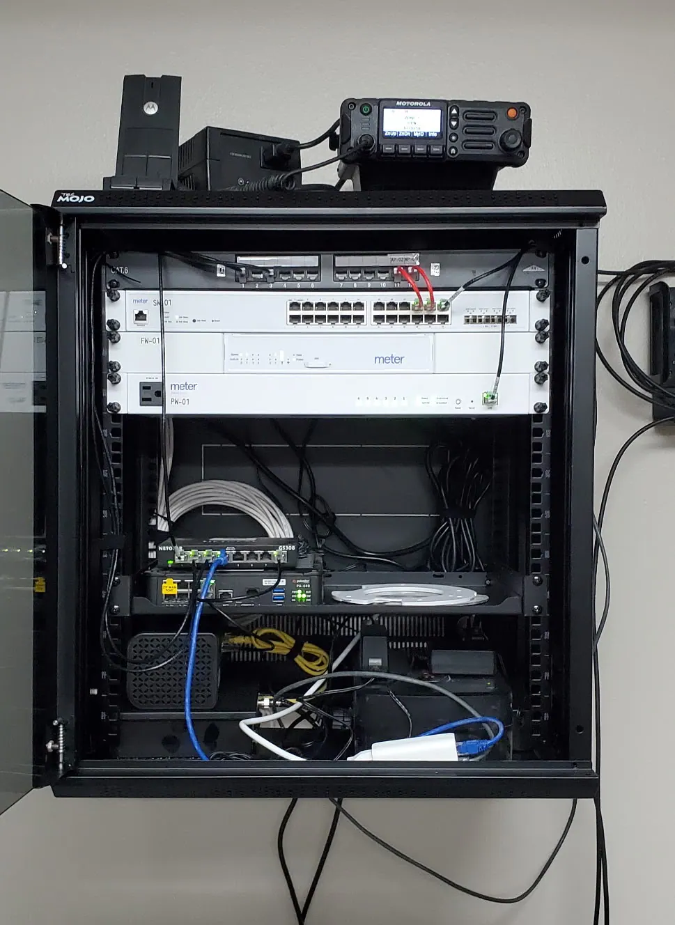 Open wall-mounted cabinet holding switches, a router and a radio