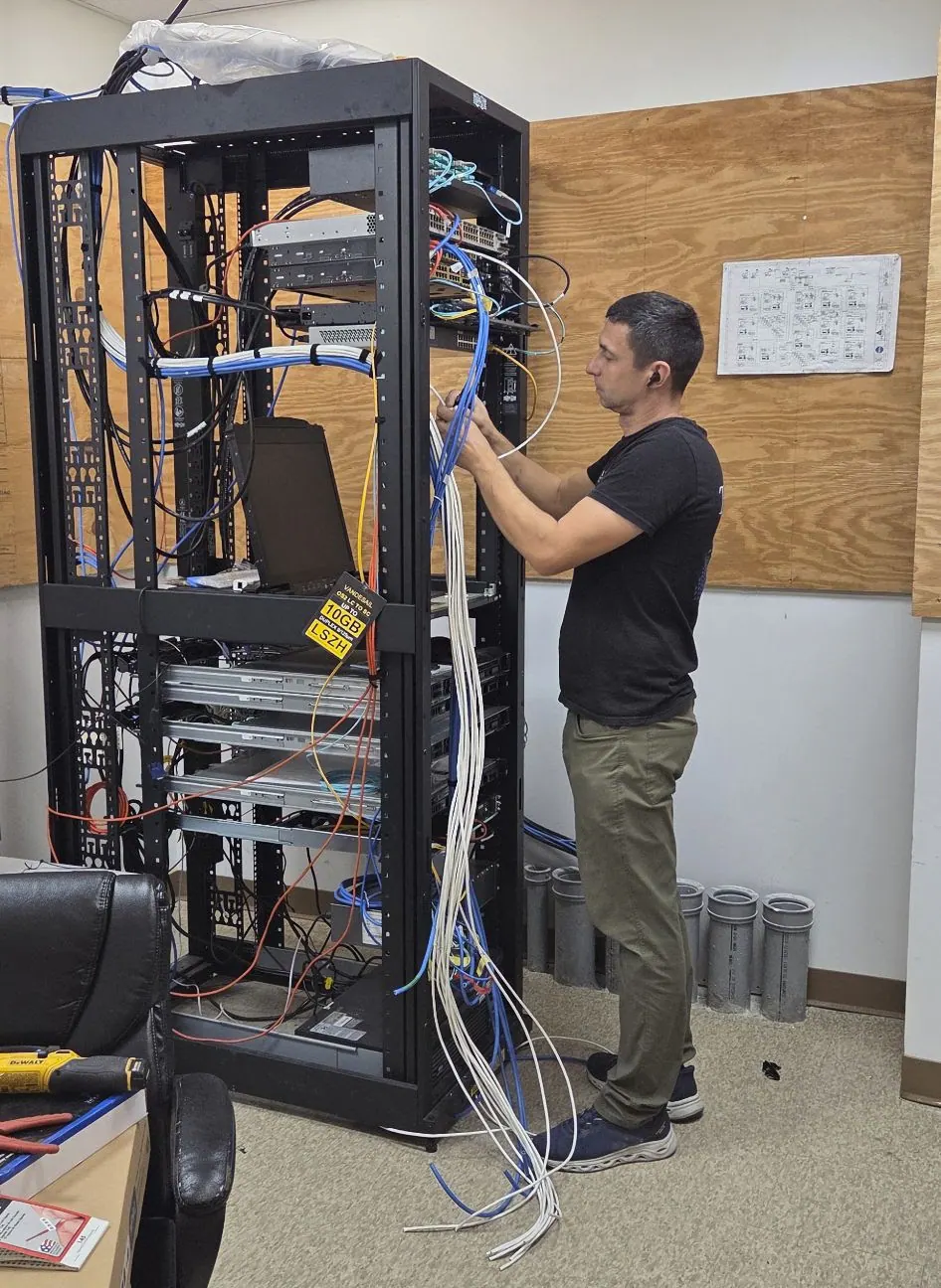 Technician in a black shirt terminating cables at a tall rack