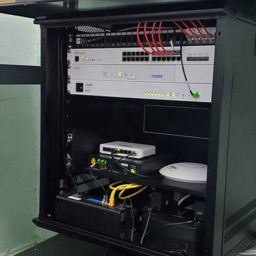 Black wall cabinet with a switch, yellow patch cables and a wireless access point