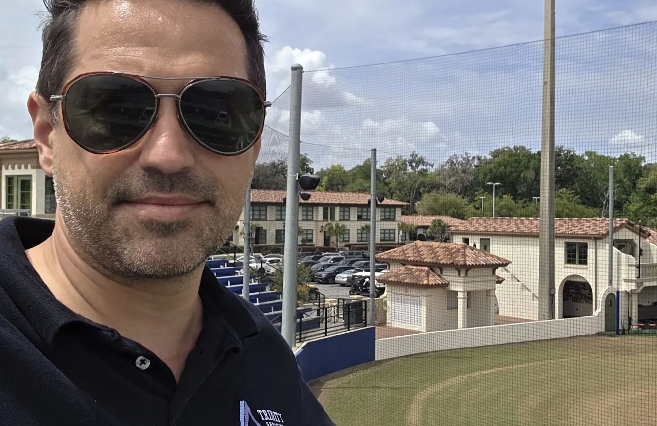 Man in sunglasses outdoors in front of a tennis court