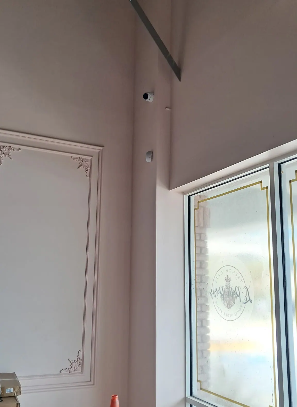 Interior wall camera above a frosted window with a gold-trim decal