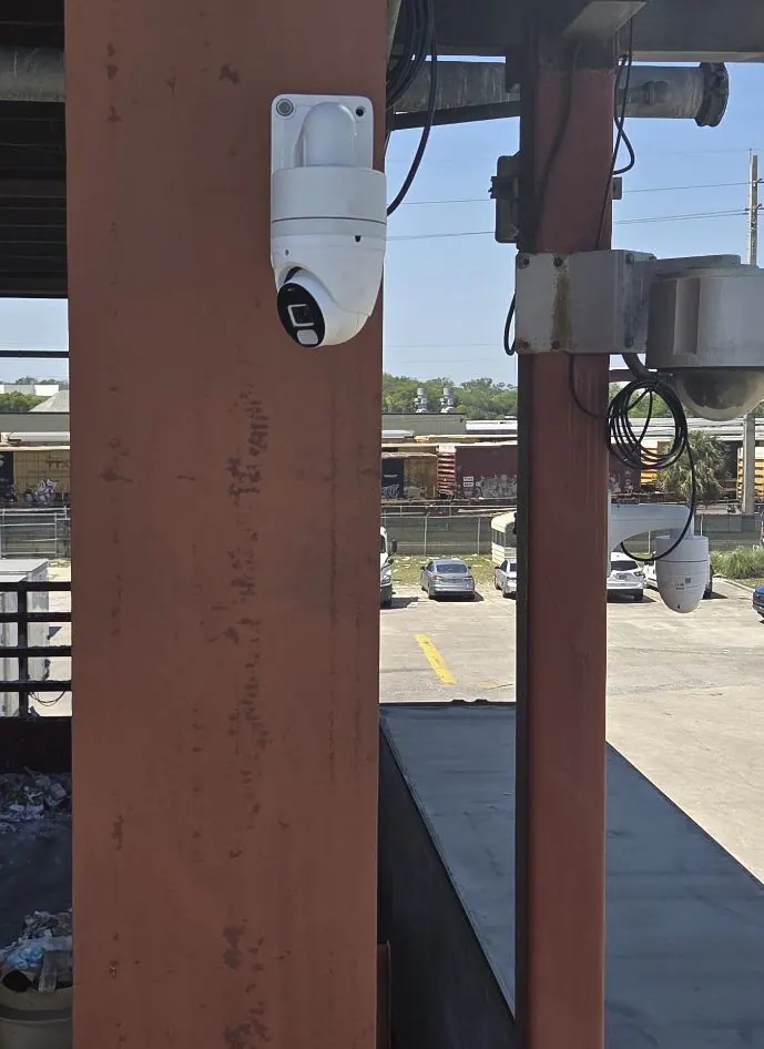 PTZ camera mounted on a rusty steel column above a parking lot