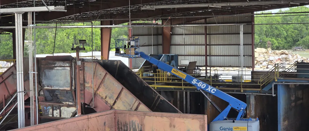 Blue boom lift beside a conveyor chute inside an industrial plant