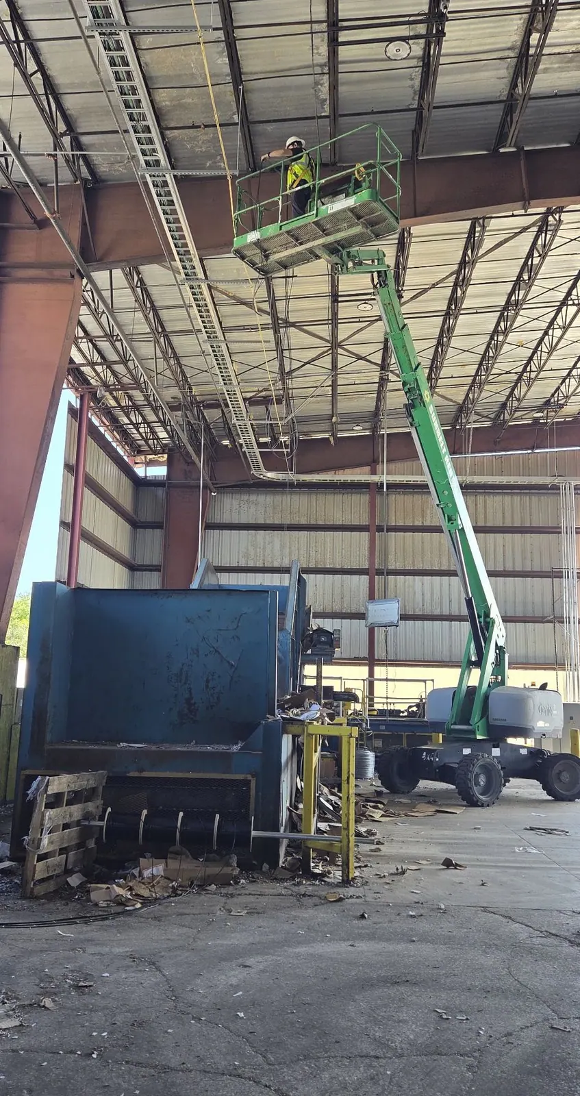 Worker in a boom lift basket beside a large hopper inside a plant